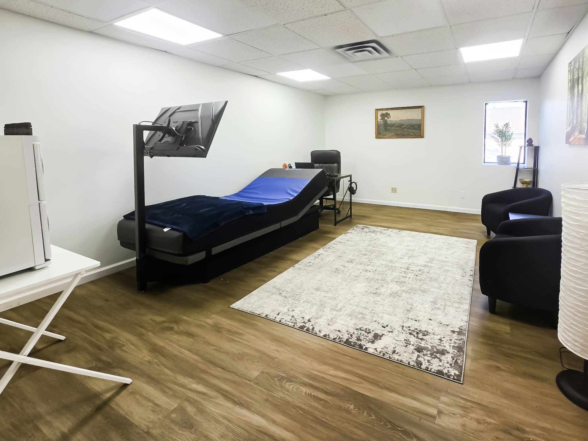 A quiet room with a reclined BioSound bed, an overhead screen, and two armchairs