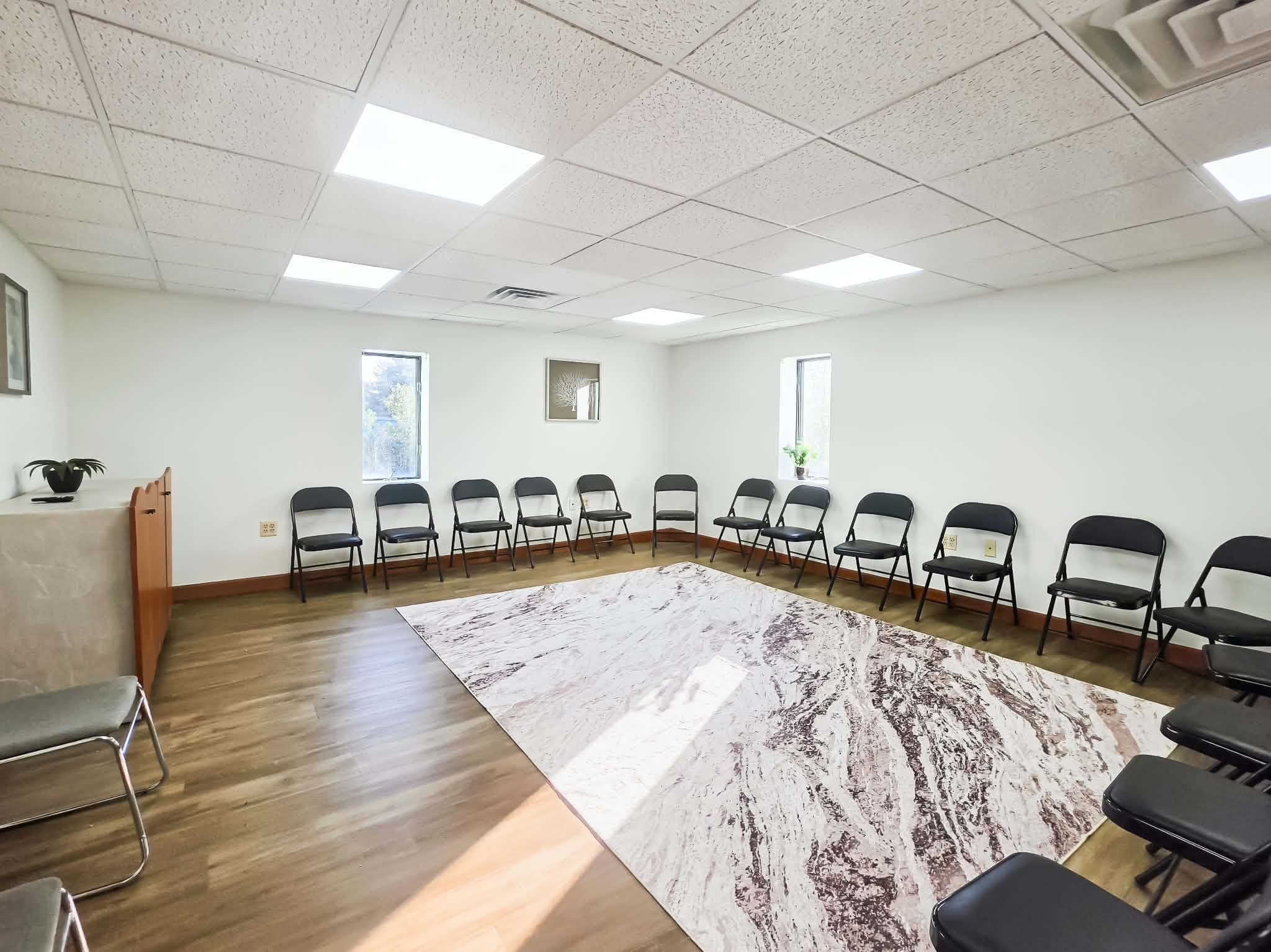 A bright group room with chairs arranged in a circle around a rug