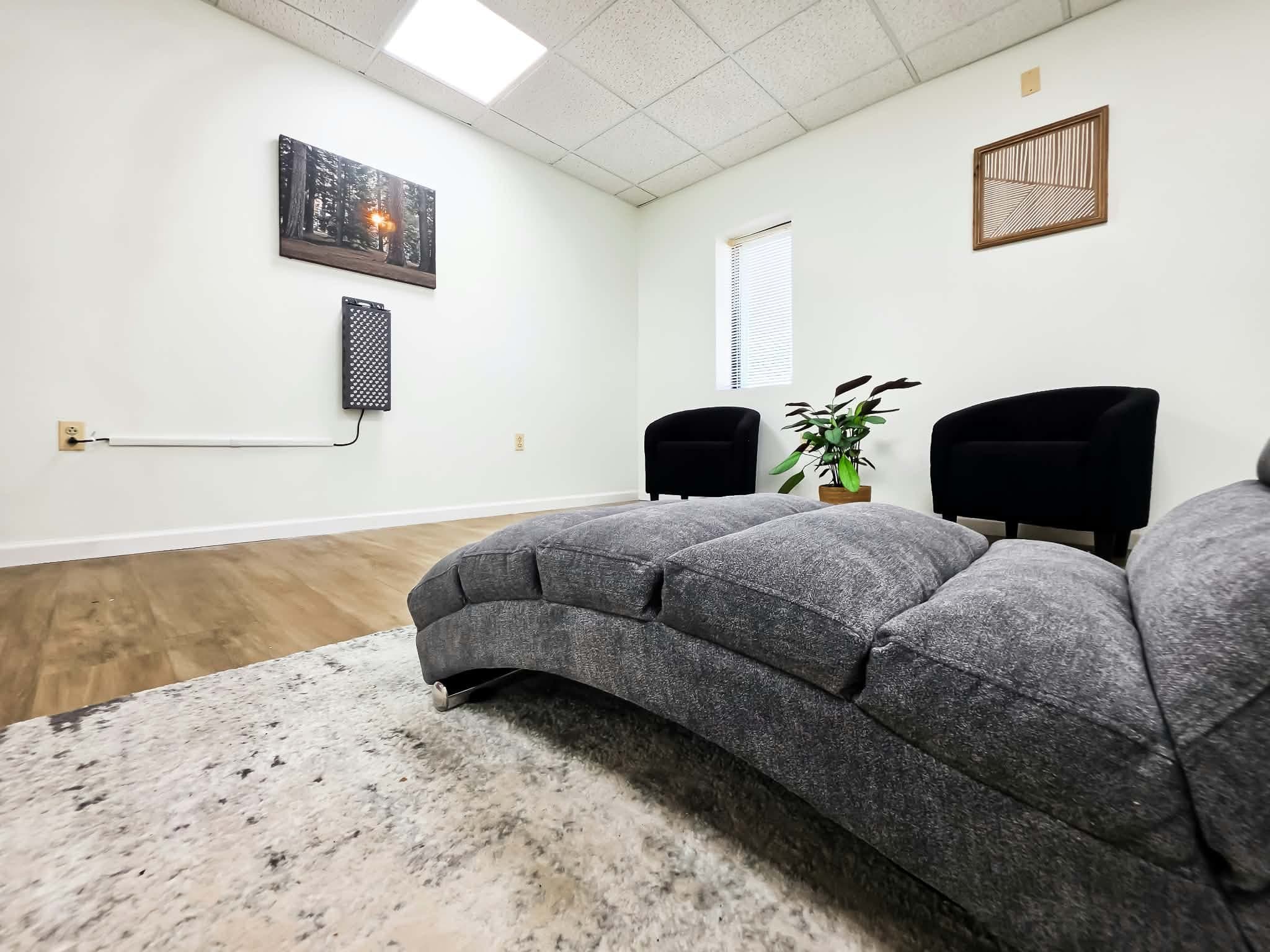 A red light therapy room with a cushioned lounge chair facing a wall-mounted light panel