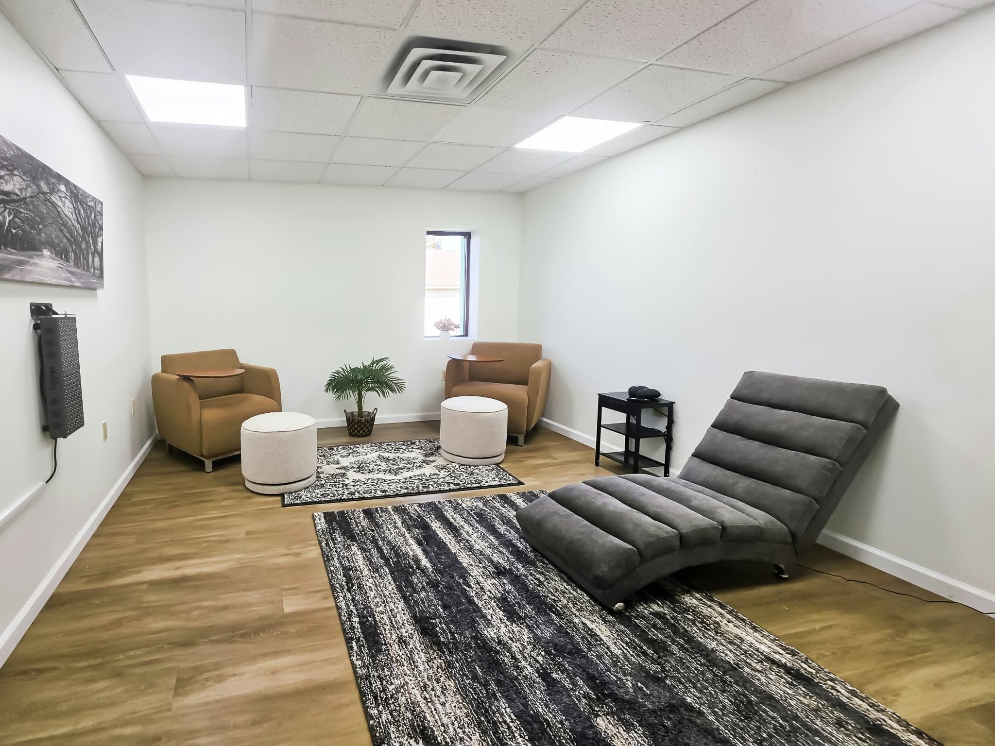 A wellness room with two armchairs, a plant, a reclining lounge chair, and a wall-mounted light panel